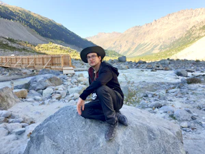 Robin Wils sitting on a rock by a glacier river, enjoying the serene view of the flowing water and surrounding nature.