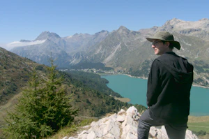 A man standing confidently on a rock overlooking a vast landscape. The Maloja Snake (clouds) is appearing between the mountains.