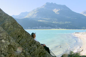 Robin Wils seated on a large rock by a lake with mountains in the background on a sunny day.