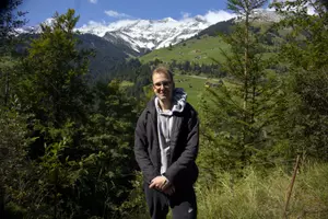 Robin standing in front of a mountain range. There are small houses on the mountain.