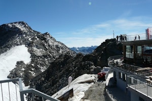 The top of a high mountain. There is snow and people are able to view it from here.