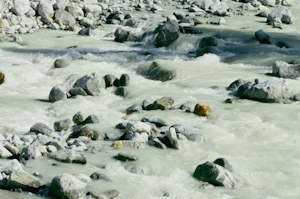Icy water of a glacier flowing against smooth rocks.