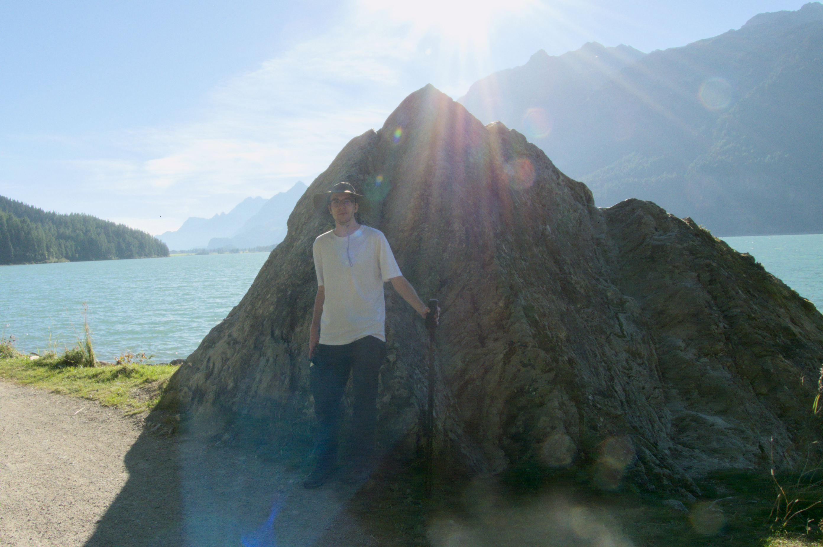 Robin Wils standing in front of the Nietzsche Stein. Blue water is behind the stone with two separate mountains.