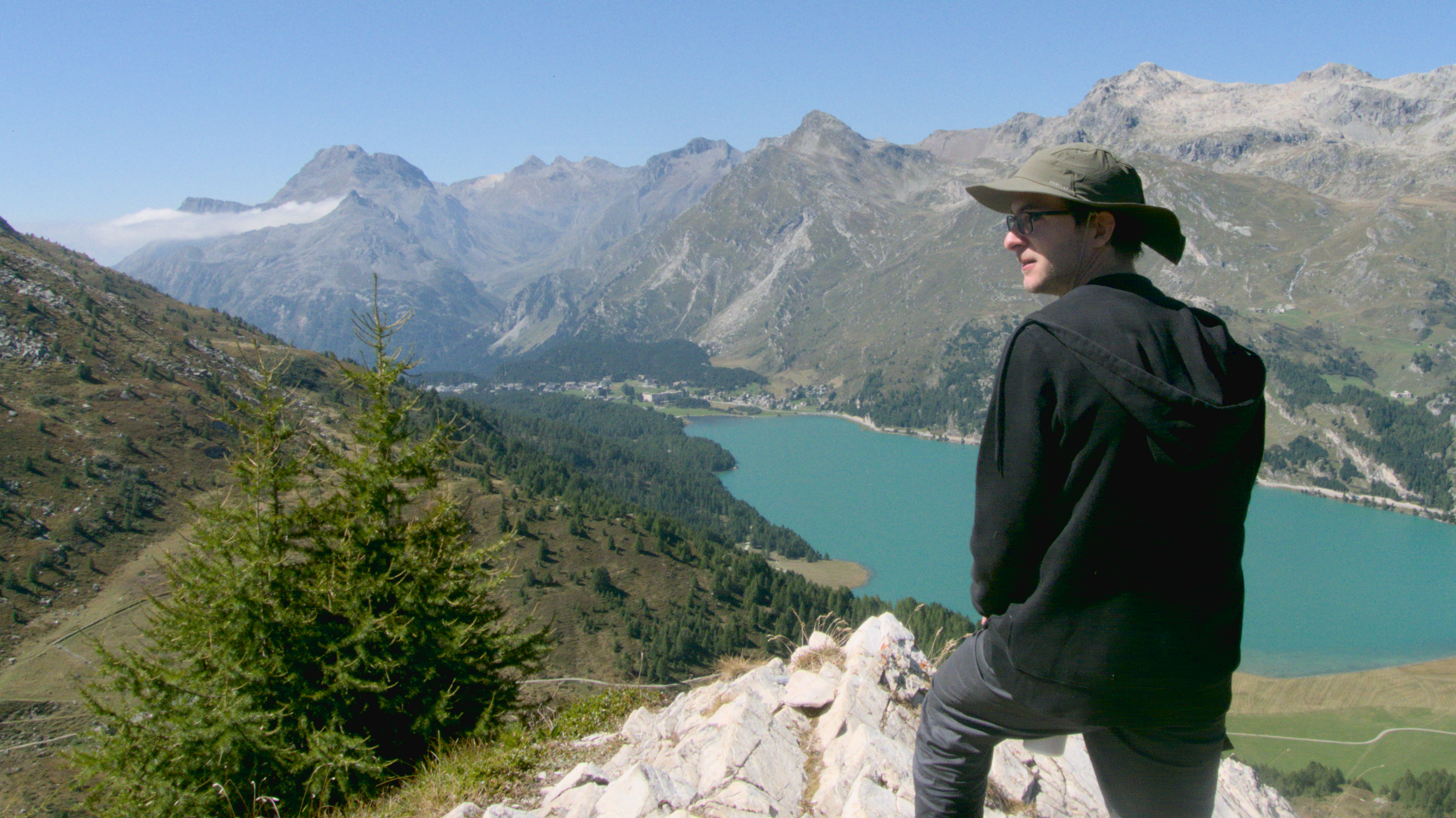 A person standing on a rock looking at a lake from a mountain in Sils-Maria.