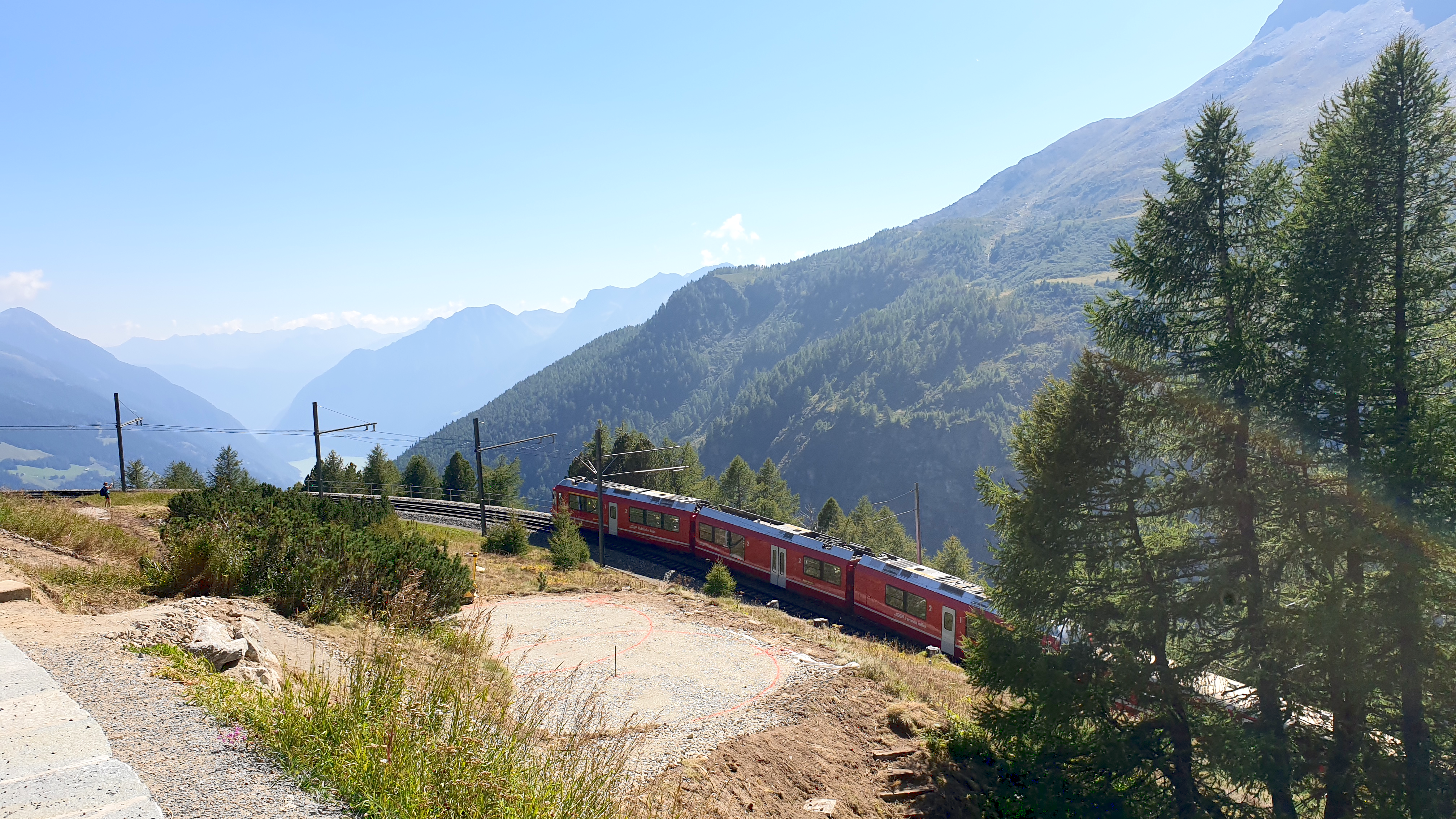 Red Swiss train against a majestic mountain backdrop.