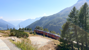 A train at a mountain range surrounded by lush greenery and winding tracks.